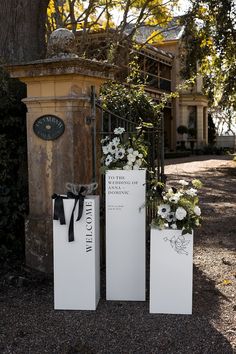 three tall white boxes with flowers in them sitting next to a tree and fenced area