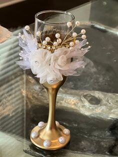 a gold vase with pearls and flowers in it sitting on a glass table next to other items