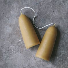 two yellow candles sitting next to each other on a gray surface with white string hanging from the top