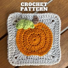 a crocheted square with an orange and green pumpkin on it, sitting on a wooden surface