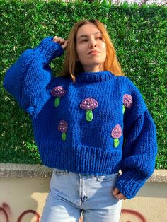 a woman is standing in front of a wall wearing a blue sweater with pink flowers on it