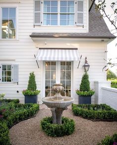 a white house with a fountain in front of it and bushes around the outside area