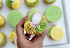 a hand holding a cupcake with a tennis racquet on top of it