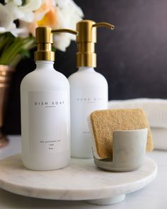 two soap dispensers sitting on top of a white marble plate next to a vase with flowers