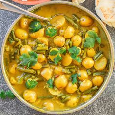 a bowl filled with potatoes and green beans next to bread on the side, topped with cilantro