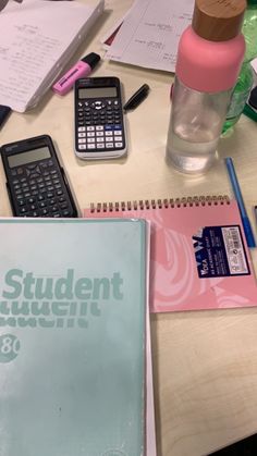 a table topped with notebooks and calculator next to a bottle of water