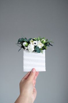 a hand holding up a piece of paper with flowers on it and greenery in the middle