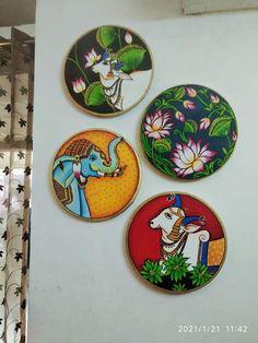 four colorfully painted coasters are hanging on the wall