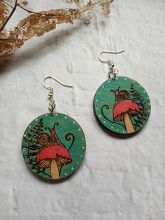 "Compliment your wardrobe with this handcrafted forest floor earrings. They are lightweight yet chunky.  Original design is drawn, woodburned and painted with acrylics and watercolors all by hand.  Earrings are sealed with 2 coats of polycrylic finish to give shine to each pendant and protect the design. Each earring is 1.5\" around and comes furnished with dangle drop ear wire. Each order comes wrapped beautifully and is ready to give. FREE SHIPPING is offered on orders over $35.  Don't hesitat Whimsical Mushroom-shaped Earrings For Gifts, Whimsical Green Jewelry With Mushroom Design, Unique Mushroom Design Earrings As Gift, Unique Mushroom Design Earrings For Gift, Green Mushroom Design Dangle Earrings, Green Dangle Earrings With Mushroom Design, Whimsical Green Mushroom Earrings, Whimsical Green Mushroom Design Earrings, Adjustable Green Mushroom Design Earrings