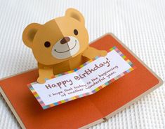 a brown teddy bear sitting on top of an orange card