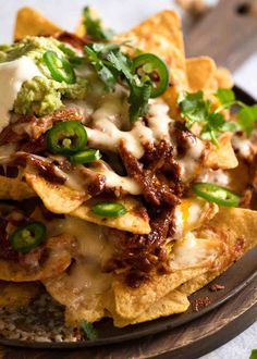 nachos with meat, cheese and green peppers on a brown plate sitting on a table