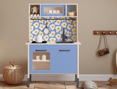 a toy kitchen with blue cabinets and yellow flowers on the wall, next to a stuffed animal