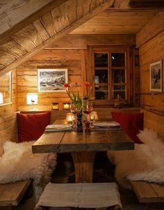 a table and benches in a room with wooden walls, wood flooring and white sheepskin rugs on the floor