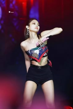 a woman in black shorts and a crop top on stage with her hand up to the side