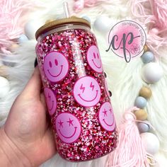 a hand holding a pink glittered cup with smiley faces on it