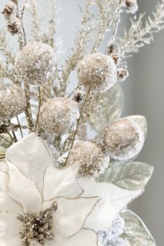 a vase filled with white flowers covered in frosted balls and leaves on top of a table