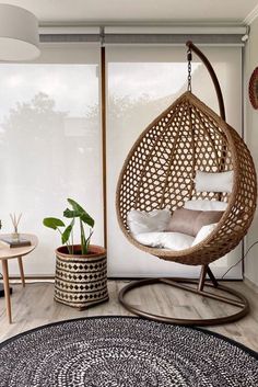 a living room with a hanging chair, rug and potted plants on the floor