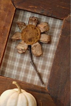 a wooden frame with a flower and two small white pumpkins in the center, on top of a plaid table cloth