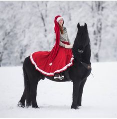 a woman in a red and white dress is riding a black horse through the snow