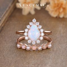 an opal and diamond ring is sitting on a wooden surface next to some flowers