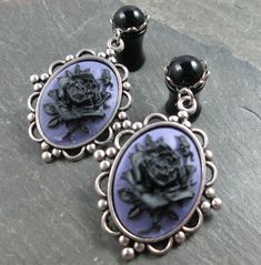 "These dangle plugs feature smooth round black gems, set in closed silver plated scalloped settings. Dangling from each is a pretty antiqued silver plated frame. The settings hold purple cameos with black roses. These would be perfect for a Gothic wedding or special occasion. These are available in the following sizes/styles: 12g (2mm) - Steel Screw Back 10g (2.4mm) - Steel Screw Back 8g (3mm) - Steel Screw Back 8g (3mm) - Acrylic Screw Back 8g (3mm) - Steel No Flare w/O Rings 6g (4mm) - Steel S Dangle Plugs, Plug Earrings, Black Gems, Acrylic Gems, Black Roses, Plugs Earrings, Gauges Plugs, Gothic Wedding, Black Acrylics