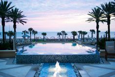 an outdoor swimming pool surrounded by palm trees and lounge chairs with the ocean in the background