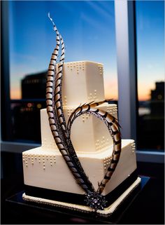 a three tiered wedding cake with an artistic design on top, in front of a window