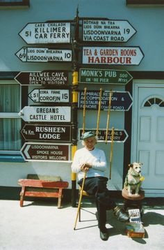 a man sitting on a chair next to a pole with street signs in front of him