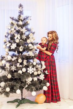 a woman holding a baby next to a christmas tree