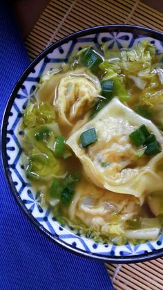 a bowl filled with dumplings and vegetables on top of a blue table cloth,