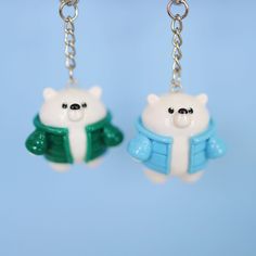 two white bears wearing blue and green clothing are hanging from silver chains on a blue background