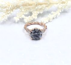 a blue diamond ring sitting on top of a white table next to some dried flowers