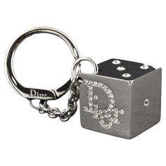 DIOR RHINESTONE GAMBLER DICE KEYRING KEYCHAIN The large square shiny reflective silver tone dice has the Dior name logo on two sides and the pips 1,2,3 and 5. Everything is set with bright clear rhinestones. A thick chain is attached to a round key holder that has a hinged lever closure. A larger size, the dice measures 1 inch square. The ring is 1 3/8 inch in diameter and the chain is 2 inches long. Color: Silver tone Material: metallic Marks: Brand mark Clasp Style: Year: 2004 Measures: 2 x 2 2000s Keychains, Dior Keychain, Accessory Inspo, Brand Mark, Silver Keychain, Cute Keychain, Cute Little Things, Essential Bag, Name Logo