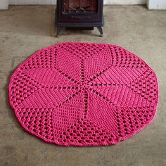 a pink crocheted rug sitting on the floor next to an old wood stove