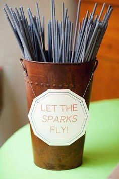 a bucket filled with lots of sticks sitting on top of a green table next to a white sign that says let the sparks fly