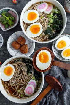 three bowls filled with noodles, hard boiled eggs and veggies next to chopsticks