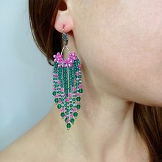 a woman wearing green, pink and white beaded earrings with flowers on the side