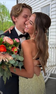 a man in a tuxedo hugging a woman in a yellow dress and holding a bouquet