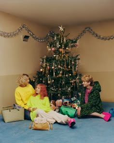 two women sitting on the floor in front of a christmas tree with presents under it