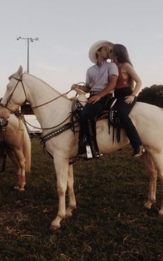 a man and woman riding on the back of white horses in a field with other horses