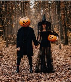 two people dressed up in halloween costumes holding hands and walking through the woods with pumpkins on their heads