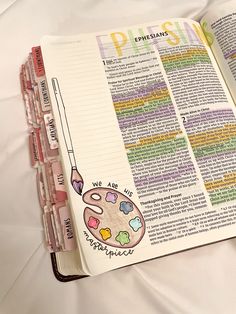 an open bible on a bed with white sheets and colorful writing in the pages,