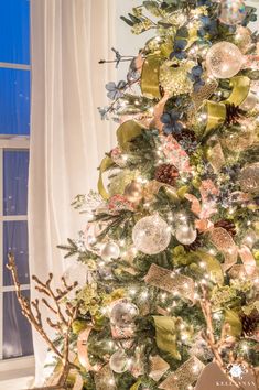 a christmas tree decorated with gold, silver and green ornaments in front of a window