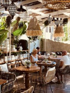 people sitting at tables in an outdoor cafe with hanging plants and potted plants on the walls