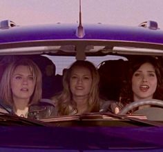 three women are sitting in the back seat of a car and one woman is laughing