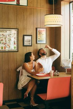 a man and woman sitting at a table in a restaurant, one pointing to the ceiling