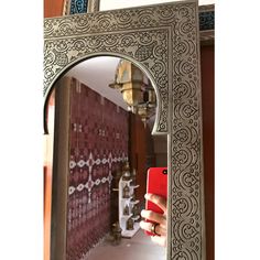 a person holding a red phone in front of an ornate silver frame with intricate designs on it