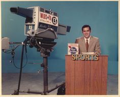 a man standing behind a wooden podium in front of a camera on a tripod