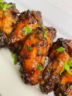 chicken wings covered in sauce and garnished with green leaves on a white plate