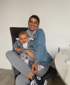 a woman sitting on a chair holding a baby in her lap and smiling at the camera